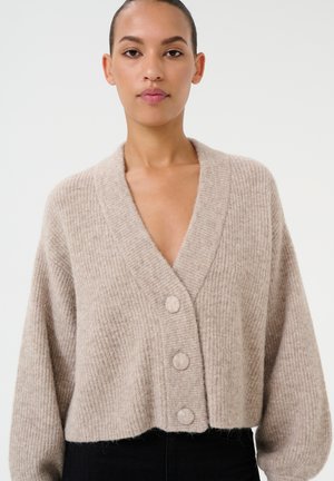 Cardigan en tricot beige avec un large col en V, trois boutons ronds et des manches longues légèrement bouffantes. Texture douce et design court.