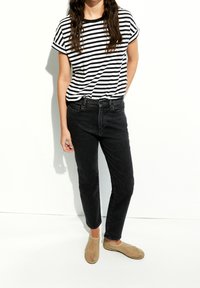 T-shirt rayé noir et blanc, jean noir et chaussures slip-on beiges. Le T-shirt a un col rond, des manches courtes et une coupe décontractée.