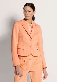 Perzikkleurige maatblazer met twee voorzakken, sluiting met één knoop en gestructureerde schouders, gecombineerd met bijpassende broek.