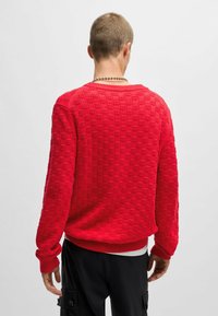 Maglione rosso lavorato a maglia con un motivo a quadri testurizzato, polsini e orlo a coste, e una vestibilità comoda. La parte posteriore mostra il design senza cuciture.
