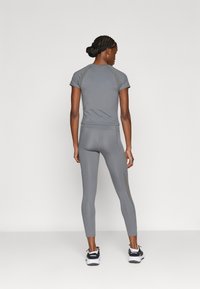 Sivi sportski komplet koji se sastoji od kratkih rukava na vrhu i uskih tajica s kontrastnim bočnim panelima. Tekstura je glatka, a kroj je strukiran.