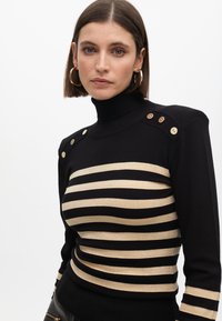 Crni i zlatni prugasti pulover s visokim ovratnikom, s prilagođenim dizajnom, koji sadrži zlatne tipke na ramenima i teksturiranu pletenu završnicu.