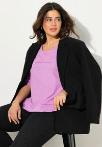 Schwarze Blazer über einem helllila T-Shirt mit dem Text "Erinnerungen sind für immer", kombiniert mit strukturierten schwarzen Hosen. Einfaches, geschichtetes Outfit.