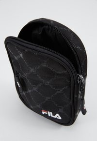 Czarna saszetka na zamek z teksturowaną powierzchnią, z delikatnym wzorem i białym logo Fila po jednej stronie.