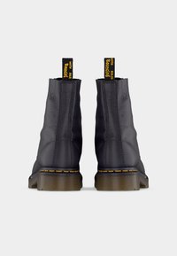 Bottes noires en cuir à cheville avec une finition mate, des coutures jaunes et des languettes de tirage. Les semelles présentent un design distinctif et rebondissant.