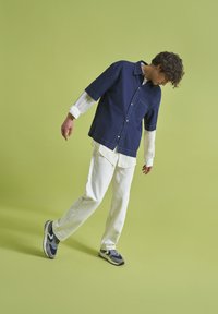 Avslappnad outfit med en marinblå kortärmad skjorta med en ficka och ett vitt långärmat lager under, tillsammans med vita byxor och flerfärgade sneakers.