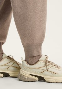 Bež joggeri s teksturom i rebrastim manžetama u kombinaciji s svijetlim tenisicama koje imaju mrežaste panele i debeli potplat.