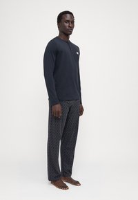 Camiseta negra de manga larga tipo henley con tapeta de botones, combinada con pantalones de pijama grises con un diseño geométrico sutil.