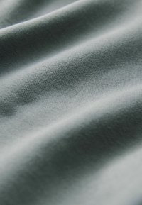 Tejido gris con textura suave, que presenta líneas sutiles horizontales y verticales. El material parece ligero y suave.