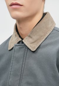 Grijze stoffen jas met een textuur van beige ribfluweel kraag, met een strak ontwerp en subtiele stiksels.