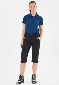 Marineblå polo shirt med korte ærmer og knaplukning, parret med sorte cropped bukser med bælte og lommer, båret med grå vandrestøvler.