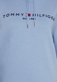 Felpa leggera blu con "Tommy Hilfiger EST. 1985" ricamato in navy e il logo a bandiera rosso, bianco e blu del marchio.