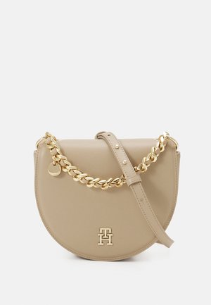 Beige halvmåneformet læderhåndtaske med en guldkæde og justerbar rem, med en guldfarvet dobbelt-T-logo foran.