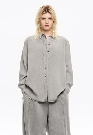 Light gray denim shirt with a button-down front, collar, and long sleeves, featuring a relaxed fit and visible seam detailing.