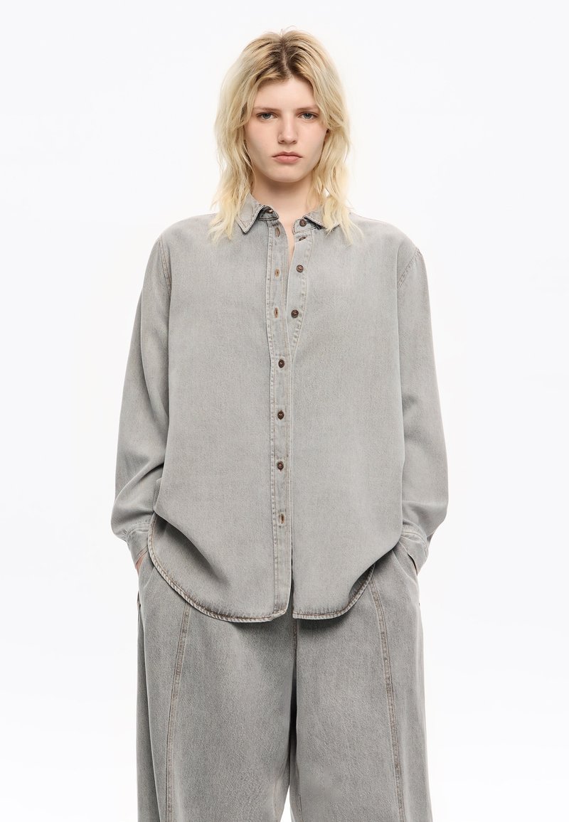Helle graue Denim-Bluse mit Knopfleiste, Kragen und langen Ärmeln, mit einem lässigen Schnitt und sichtbaren Nahtdetails.