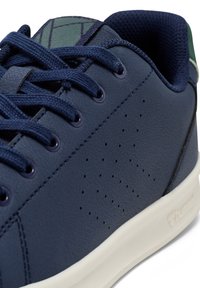 Marinblå syntetiska sneakers med en texturerad övre del, rund tå, perforeringar för andningsförmåga och en vit gummisula.