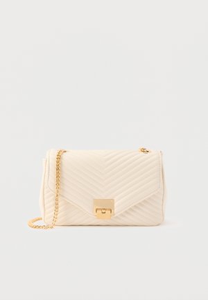 Sac à main en cuir matelassé couleur crème avec une sangle à chaîne dorée et un fermoir rectangulaire doré sur un fond uni.