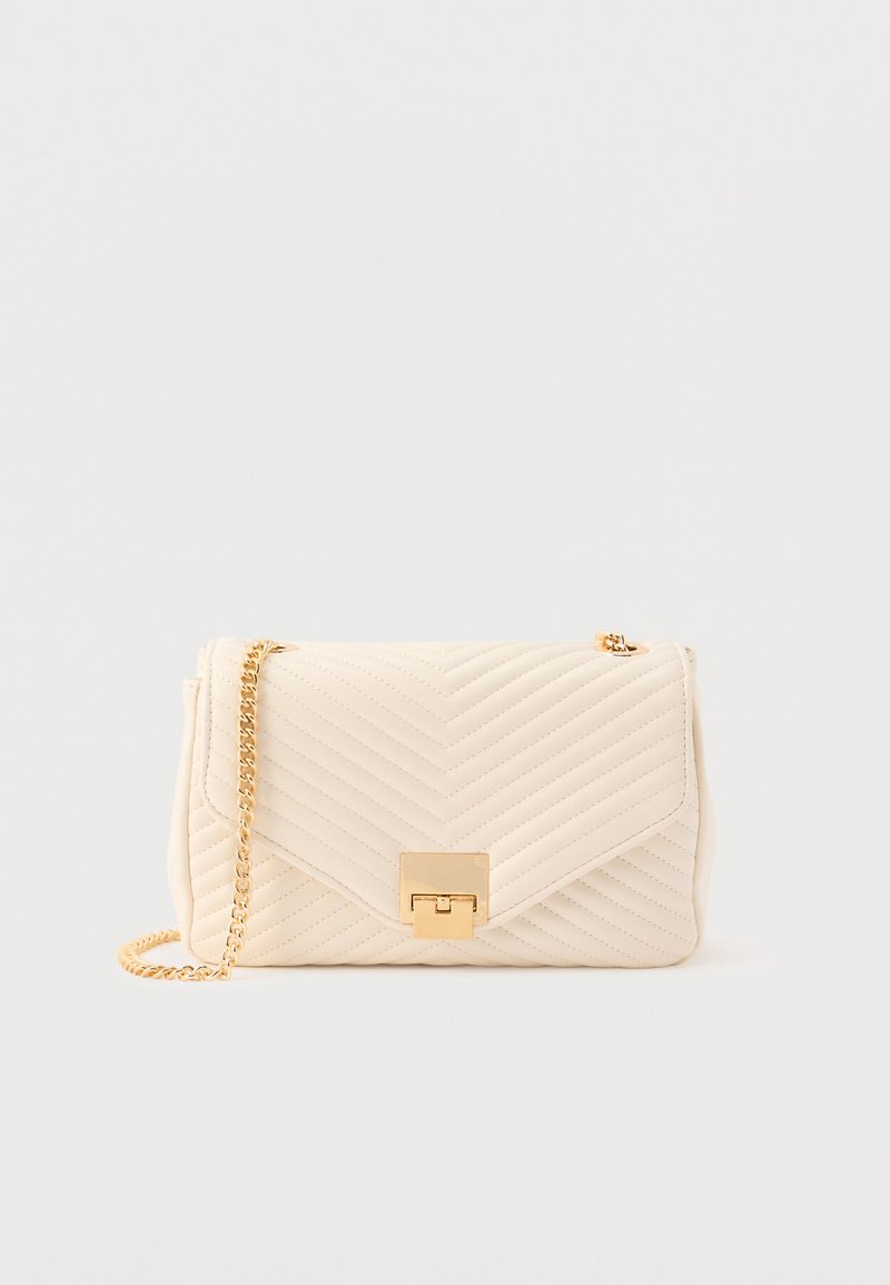 Sac à main en cuir matelassé couleur crème avec une sangle à chaîne dorée et un fermoir rectangulaire doré sur un fond uni.