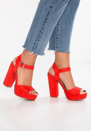 Sandalias de tacón alto de ante rojo con plataforma, punta abierta y correa en el tobillo. Tacón grueso y macizo con acabado liso.