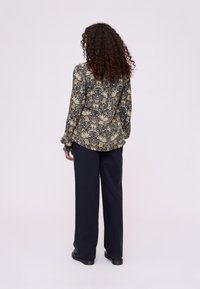 Blouse à manches longues avec un motif floral bleu foncé, en tissu léger, associée à un pantalon noir à jambes larges et des chaussures noires.
