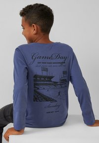 Langärmliges blaues T-Shirt mit einem schwarzen Grafikdruck eines Sportstadions und Text, aus Baumwollmaterial, Rundhalsausschnitt und lässiger Passform.