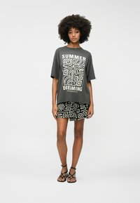T-shirt gris oversize avec un graphique blanc "SUMMER DREAMING" ; associé à un short noir avec des motifs abstraits blancs ; sandales noires à lanières.