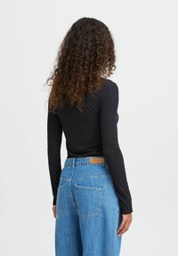 Black ribbed long-sleeve top paired with light blue high-waisted jeans featuring a leather label, designed with a relaxed fit and two back pockets.