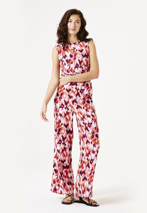 Jumpsuit floral coloré en tissu léger avec jambes larges, présentant des nuances de rouge, rose et blanc. Comprend un design sans manches et une ceinture.