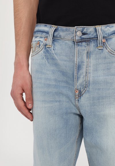 Gai zila džinsu bikses ar taisnu piegriezumu, piecu kabatu dizainu un vara pogu. Mazliet nolietota tekstūra tuvu kabatām.