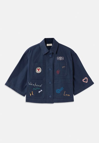 Navy blue short-sleeve shirt with button closure, featuring various embroidered patches, including hearts and text. Includes chest and side pockets.