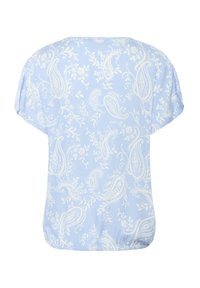 Light blue short-sleeve blouse with a paisley pattern in white. Soft fabric, rounded hem, and elastic gathering at the bottom.