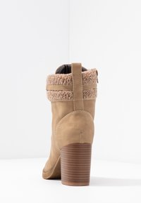 Beżowe zamszowe botki za kostkę z sztucznym futrem na górze, solidnym, zaokrąglonym obcasem i zamkiem błyskawicznym z boku. Teksturowany obcas podkreśla design.