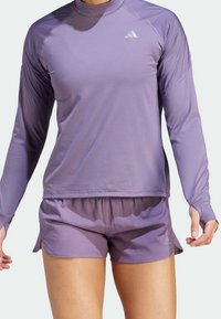 Langdurige mouw paarse sporttop met een ronde halslijn en textuurstof; gecombineerd met bijpassende paarse shorts, beide gemaakt van lichtgewicht materiaal.