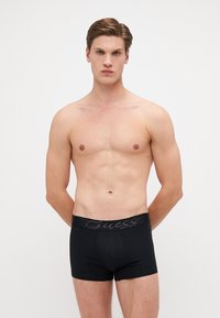 Sorte boksertruser med en glatt tekstur og en merket elastisk midje. Tettsittende design, midt-lår lengde, og ingen ekstra mønstre.