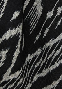 Tessuto in bianco e nero con un pattern irregolare e astratto a strisce, simile a pennellate, che mostra texture e pieghe.