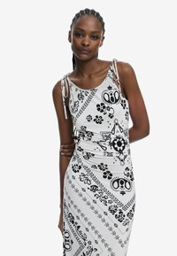 Weißes ärmelloses Kleid mit schwarzen Blumen- und abstrakten Mustern, verstellbaren Trägern auf den Schultern und einer figurschmeichelnden Passform.