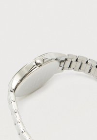 Sudrabota roku skatīšanās ar apaļu korpusu un savienoto aproci, parādīta no sāna, akcentējot kroni uz balta fona.