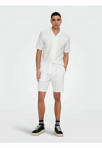 White short-sleeve shirt and matching shorts in lightweight fabric. Features a button-up front, and worn with black sneakers and striped socks.
