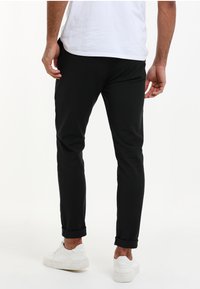 Black slim-fit pants with a smooth texture, cuffed hems, and side pockets. Worn with a white shirt and white sneakers.
