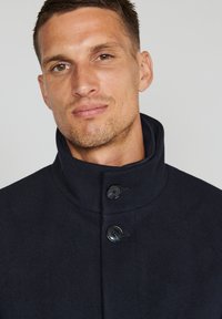 Abrigo de mezcla de lana de color marino con un cuello alto, dos botones frontales y una textura suave. Diseño minimalista sin patrones o acentos visibles.