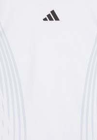 Bijela atletska majica od glatkog materijala, s crnim Adidas logotipom i suptilnim sivim zakrivljenim linijama uz strane.