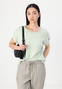 T-shirt rayé vert clair avec un col arrondi et des manches retroussées, associé à un pantalon beige à taille élastique et à un petit sac à main noir.