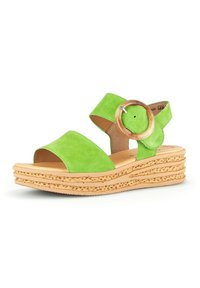 Sandal verde in suede con fasce larghe e un dettaglio rotondo in legno. Presenta una suola in sughero stratificato e texturizzato per maggiore altezza e comfort.