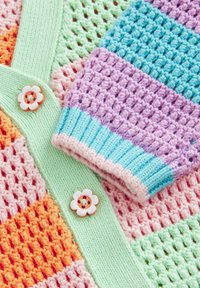 Vêtement coloré tricoté et crocheté avec des rayures pastel et des boutons en forme de fleurs sur une base tricotée vert clair.