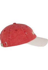 Rdeča bombažna kapica z belim vizirjem. Ima zbledelo teksturo, nastavljiv trak na hrbtni strani in izvezeno "NE". Oprane podrobnosti na vizirju.