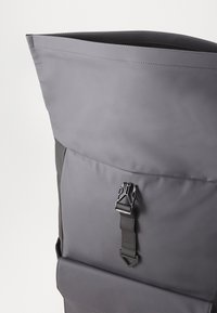 Gray roll-top backpack made of weather-resistant material, featuring a sturdy black buckle and a smooth texture with visible stitching details.