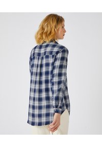 Camicia a quadri blu navy e bianca con maniche lunghe, yoke posteriore, polsini a bottoni e orlo curvo. Realizzata in un tessuto morbido con una superficie liscia.
