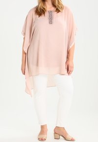 Ljusrosa chiffonblus med korta ärmar och en texturerad pärlkrage, kombinerad med vita byxor och nude blockklacksandaler.