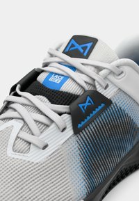 Close-up of gray athletic shoe with blue accents and white laces tied in a lace tuck design on the tongue and side panel.
