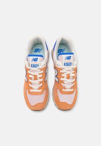 Orange mocka och rosa tyg sneakers med vita snören, blå detaljer och en '574' etikett på tungan. Klassisk löparskodesign.